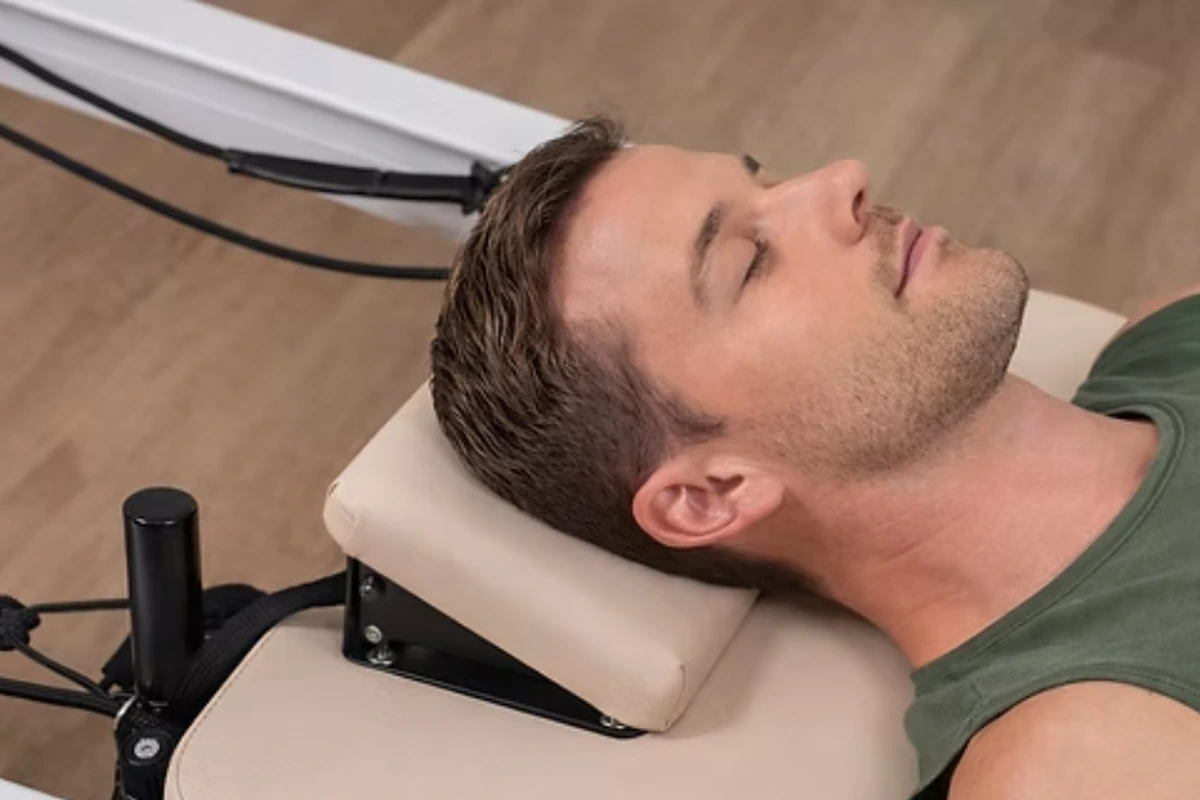 Pratiquant installé sur l’appui-tête d’un Reformer Pilates
