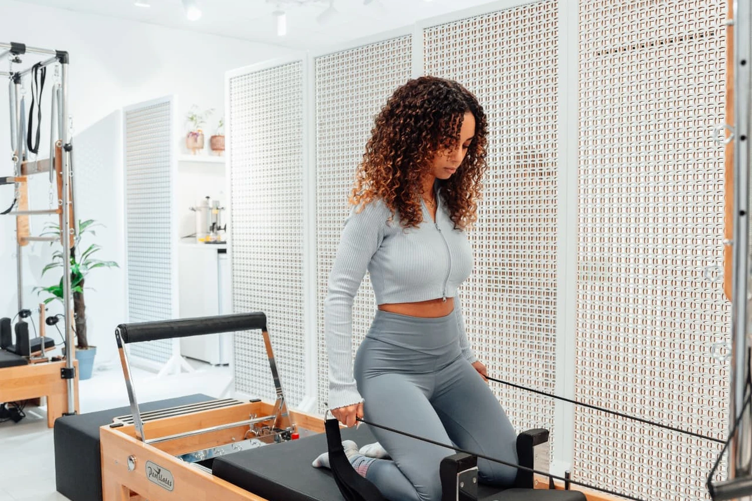 Pratiquante testant un Reformer Pilates en bois dans un studio lumineux