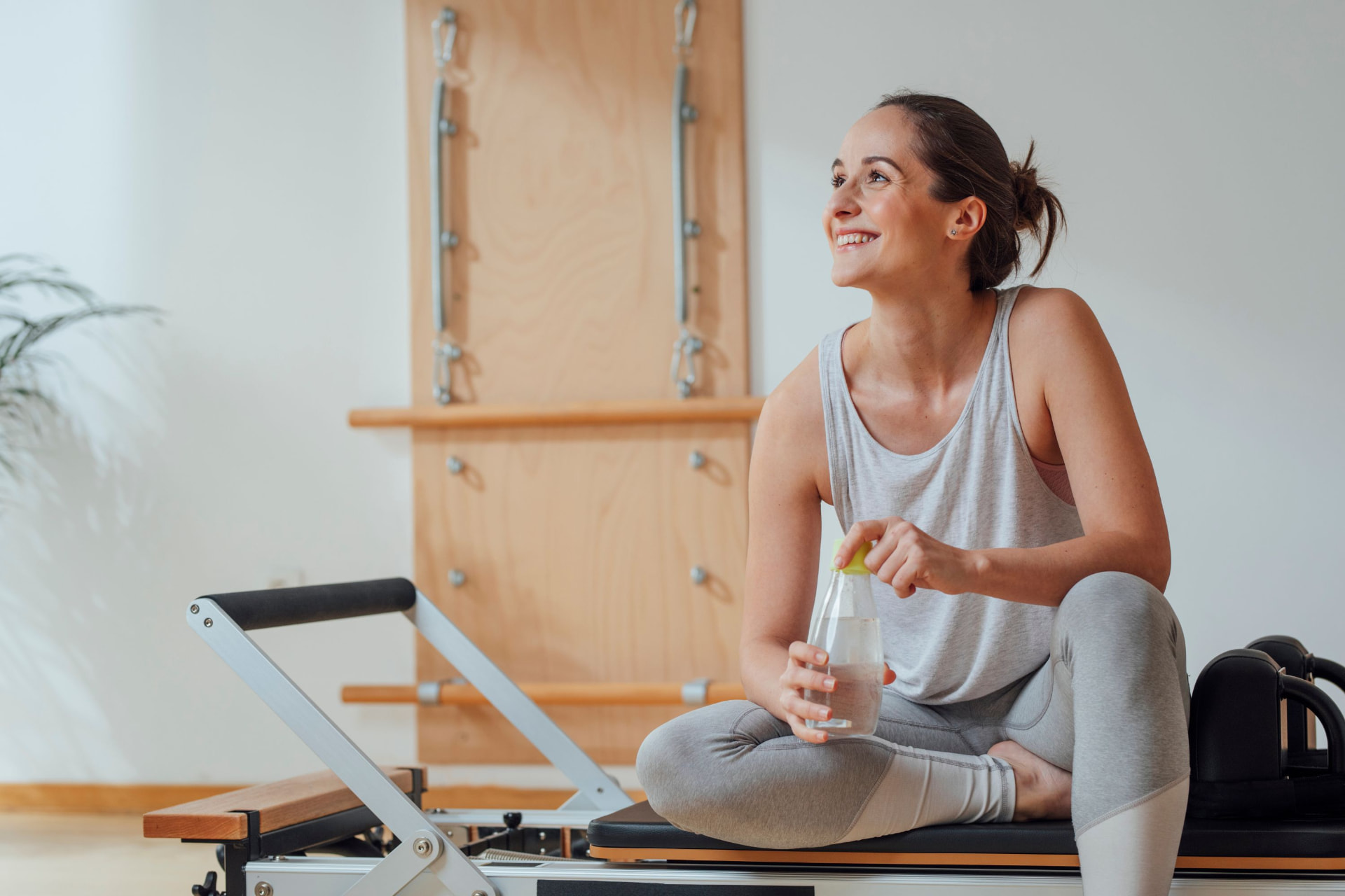 Pratiquante souriante assise sur un Reformer Pilates dans un studio lumineux